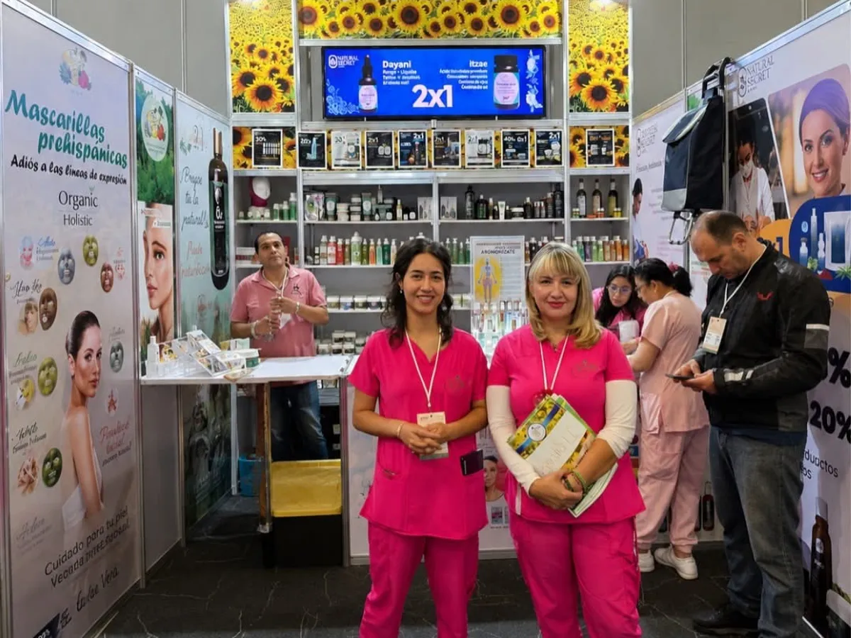 Expositoras atendiendo su stand de cosmética profesional, con el anaquel de producto y visitantes alrededor, durante la Expo